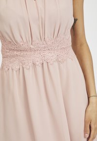 Rosa Chiffonkleid mit einem Spitzenbund und floralen Mustern. Der Stoff ist weich und fließend, betont die Taille.
