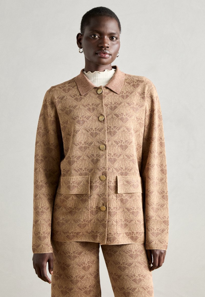 Braun gemusterte Jacke mit Kragen, vorderen Taschen und Knopfverschluss. Strukturierter Stoff ergänzt die passende Hose.