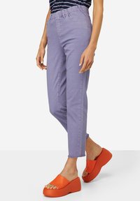 Jeans elásticos de color lavanda con una cinturilla acanalada, ajuste tipo taper y dobladillos deshilachados en los tobillos. Combinados con sandalias de plataforma naranjas.
