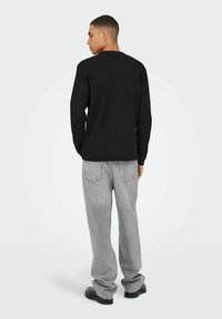 Sort ribbet langærmet skjorte i kombination med løstsiddende lys grå jeans og sorte sko, set fra ryggen. Enkel design, ingen mønstre.