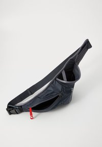 Siva crossbody torba izrađena od lagane tkanine, s glavnim odjeljkom, bočnim zip džepom, podesivim remenom i detaljem crvene munje.