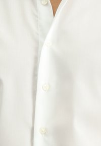 Camicia bianca con bottoni in un tessuto liscio, caratterizzata da bottoni simili a perle e un design a colletto classico, che mette in evidenza linee pulite e un look sartoriale.