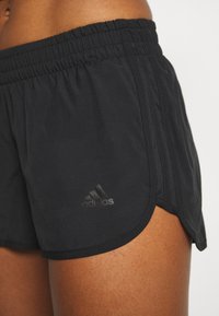 Svarta idrottsshorts med elastisk midja, med en subtil Adidas-logotyp i en mörkare nyans. Slät, lättviktig tyg; något rundad fåll.
