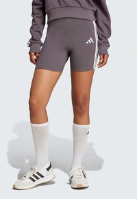 Γκρι αθλητικά σορτς με λευκές ρίγες στο πλάι και λογότυπο Adidas. Συνδυάζονται με λευκές κάλτσες μέχρι το γόνατο και αθλητικά παπούτσια. Λείο υλικό.