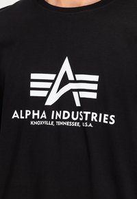 Tricou din bumbac negru, cu un logo grafic alb mare, cu dungi și textul "ALPHA INDUSTRIES" și "KNOXVILLE, TENNESSEE, U.S.A."