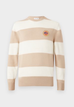 Bež in bela črtasta pletena pulover, krojenega vratu, z rebrastimi manšetami in robom. Na prsih ima okrogel vezen logotip.