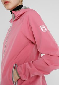 Roze waterdichte jas met een ritssluiting aan de voorkant, grijze voering, elastische manchetten en zijzakken. Voorzien van een logo-opdruk op de linkerarm.