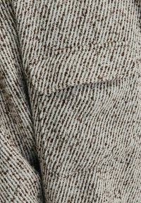 Wzorzysty kawałek materiału w off-white z brązowymi paskami, z kieszenią łataną. Materiał to mieszanka wełny z deseniem w jodełkę.