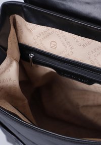 Interior de un bolso de mano de cuero negro con forro de tela beige, que cuenta con un bolsillo con cremallera y un patrón de logotipos repetido en el forro.