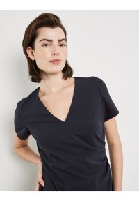 Marineblaues Kleid mit kurzen Ärmeln und V-Ausschnitt. Weicher Stoff, taillierte Passform, mit gerafften Details an der Taille.