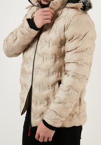 Beige puffer jacket with a zip front, hood, and elastic cuffs. Features a smooth, shiny texture with a puffy, quilted design and side pockets.