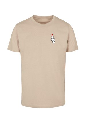 Beige puuvillane T-särk, millel on trükitud kujundus käest, mis teeb südame žesti, käe sõrmede kohal on väike punane süda.