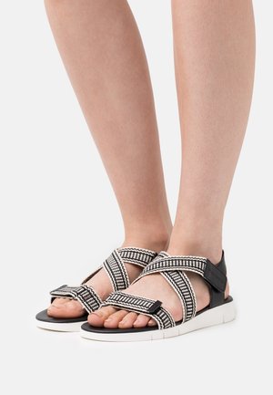 Sandalias de tiras en blanco y negro con un patrón trenzado, correas ajustables y una suela acolchada con una suela exterior de goma blanca.