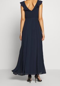 Mörkblå maxiklänning i lätt tyg, med V-rygg, volangärmar och en flödande silhuett, i kombination med svarta klackar.