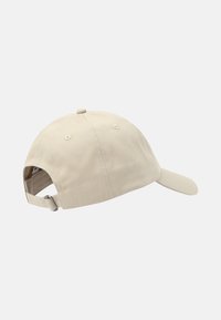 Gorra de algodón beige con visera curvada, correa ajustable en la parte posterior y corona redondeada. Presenta orificios de ventilación y un diseño sin costuras.
