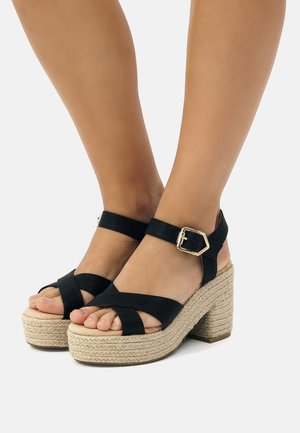 Sandalias de plataforma negras con suela de yute trenzado, correas cruzadas y una hebilla ajustable. Material suave y altura de tacón moderada.
