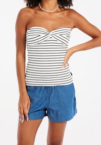 Strapless top in white with black stripes, featuring a twist detail at the bust. Paired with blue cargo-style shorts made of lightweight fabric.