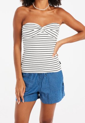 Strapless top in white with black stripes, featuring a twist detail at the bust. Paired with blue cargo-style shorts made of lightweight fabric.