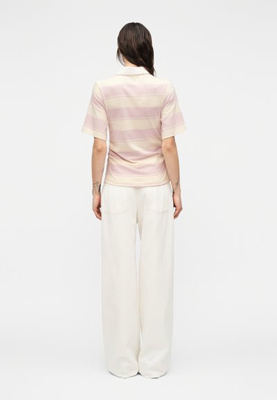 Ριγέ πόλο μπλουζάκι σε απαλό ροζ και κρεμ βαμβακερό μείγμα, με κοντά μανίκια και κλασικό γιακά, συνδυασμένο με άνετο λευκό παντελόνι.