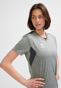 Grå sportst-shirt av texturerat tyg med korta ärmar, V-ringning, svarta sidodetaljer och en logotyp på bröstet.