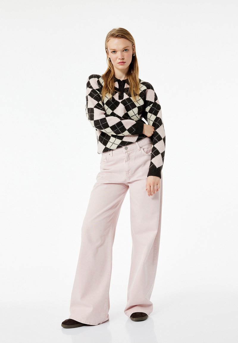 Schwarzer und rosa Argyle-Pullover mit rundem Ausschnitt kombiniert mit hellrosa weiten Hosen. Das Outfit hat einen lässigen, entspannten Sitz.