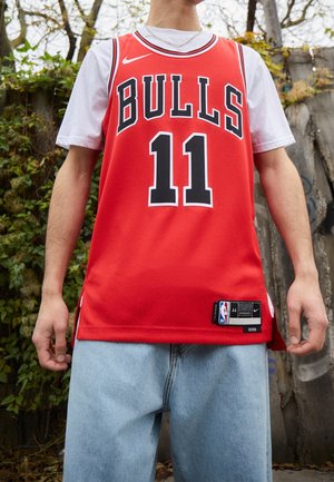 Person iført en rød Chicago Bulls basketballtrøje nummer 11 over en hvid t-shirt og lyseblå jeans udendørs.