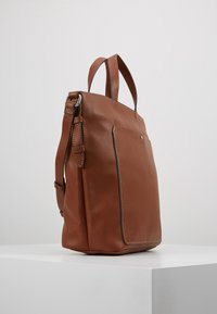 Tote bag en cuir marron texturé avec deux anses supérieures, une bandoulière réglable et une poche avant. Lignes épurées et design fonctionnel.