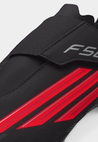 Μαύρο παπούτσι ποδηλασίας με κόκκινες διαγώνιες ρίγες και μαύρη ταινία Velcro στην κορυφή με την επιγραφή «F50».