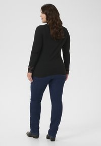 Top nero a maniche lunghe con dettagli in pizzo sulle maniche, abbinato a jeans blu scuro. Finitura in tessuto liscia, design semiaderente e orlo curvo.