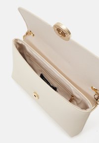 Pochette couleur crème avec un extérieur lisse, une quincaillerie dorée et une fermeture à pression. Comprend une poche intérieure et une doublure douce.