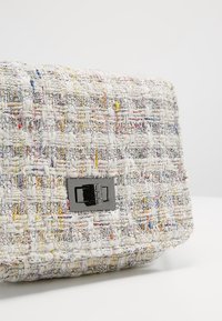 Borsa in tweed con fili multicolori. Superficie texture, forma rettangolare, presenta una chiusura in metallo nero e una patta pieghevole.