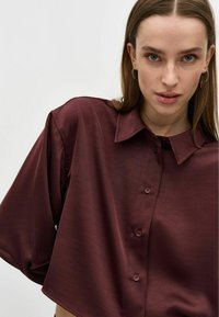 Bordowa, oversize bluzka z kołnierzykiem, krótkimi rękawami i zapięciem na guziki, wykonana z gładkiego, lekkiego materiału.