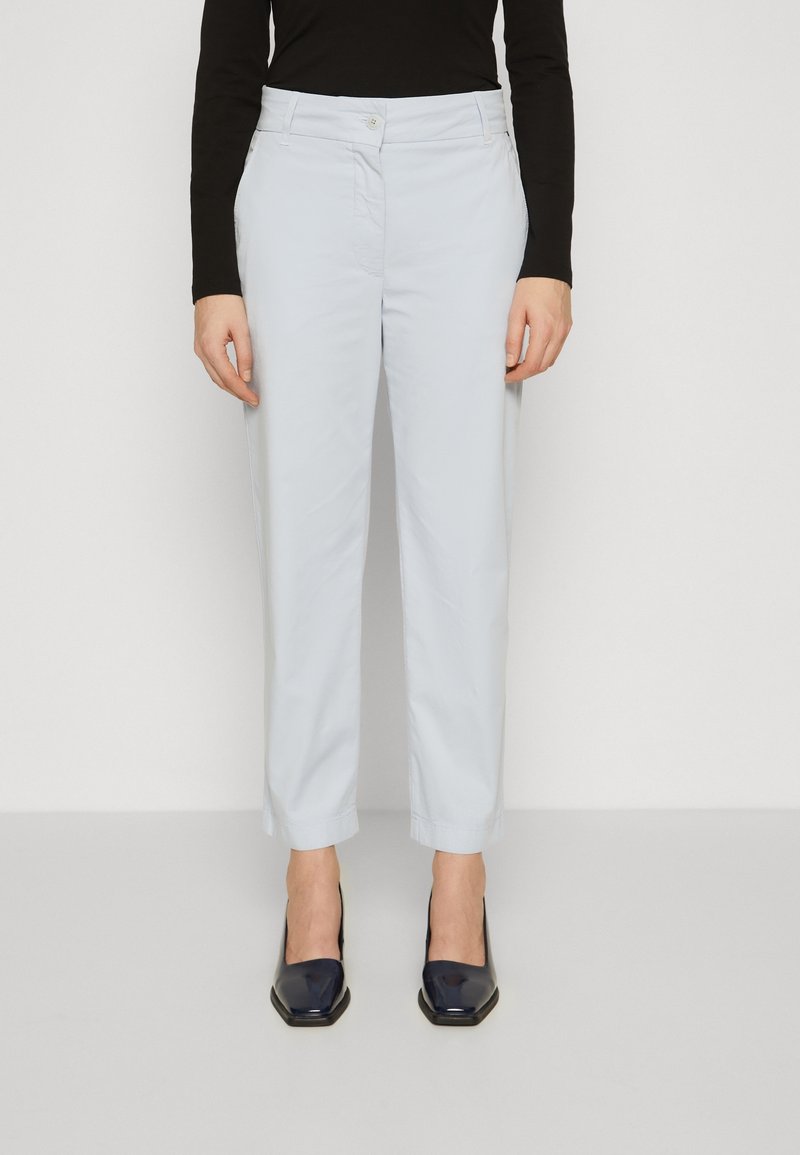 Pantaloni azzurri chiari realizzati in un tessuto morbido, con un design a gamba dritta e chiusura con bottone. Indossati con tacchi quadrati scuri e lucenti.