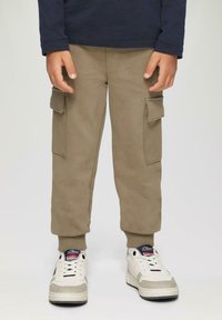 Cargo-Hosen aus hellbraunem Baumwollstoff, mit Seiten Taschen und gerippten Knöchelabschlüssen, kombiniert mit weißen Sneakers mit grauen Akzenten und logoversehener Zunge.