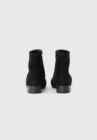 Schwarze Wildleder-Stiefeletten mit glatter Oberfläche, runder Zehenpartie und niedrigem Blockabsatz. Seitlicher Reißverschluss für einfaches An- und Ausziehen.