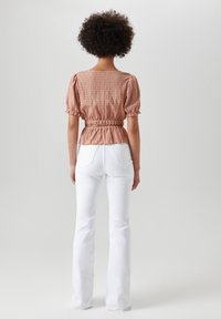 Bluse mit Pfirsichmuster, puffärmelig und mit gerafftem Bund, kombiniert mit weißen, ausgestellten Jeans. Glatte Textur, lässiges Design.