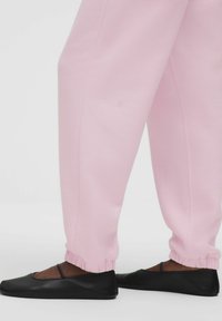 Rózsaszín sportnadrág rugalmas mandzsettákkal, fekete balettcipőkkel párosítva, sima textúrával és minimalista dizájnnal.