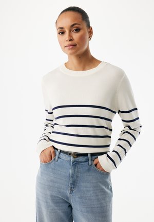 Suéter de punto blanco con rayas horizontales azul marino, cuello redondo y puños acanalados, combinado con pantalones vaqueros de tiro alto en azul claro.