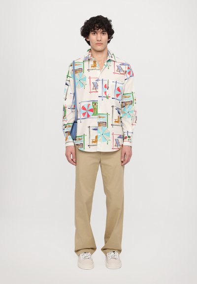 Button-up shirt made of fabric featuring a multicolored beach-themed print, paired with beige trousers and white sneakers.