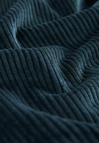Tissu en velours côtelé bleu foncé avec des côtes visibles et des plis doux créant un motif texturé et ondulé.