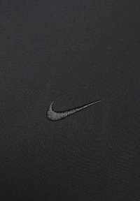 Zwarte stof met een gladde textuur, met een tonale, geborduurde Nike Swoosh-logo, opvallend in het midden geplaatst.