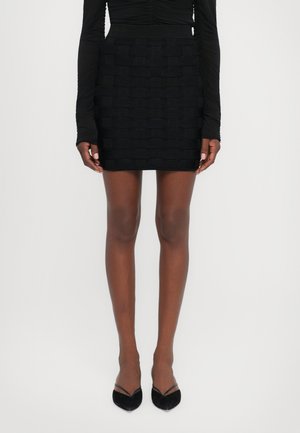 Black mini skirt with a textured, woven pattern. Stretchy fabric, fitted silhouette, and a smooth waistband. Paired with black pointed heels.