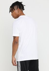 T-shirt sportivo bianco con maniche corte, scollatura rotonda e pannello laterale in rete traspirante, abbinato a pantaloni sportivi neri.