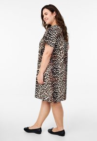 Sukienka z krótkim rękawem w deseń panterki o luźnym kroju, wykonana z lekkiego materiału. Zestawiona z płaskimi czarnymi butami.
