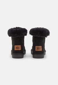 Botines negros de ante con forro de pelo sintético. Presentan un parche de logo marrón y una suela de goma texturizada. Diseño de tacón plano.