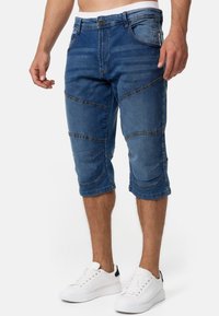 Shorts din denim de culoare albastră, cu o croială până la genunchi, având detalii din panouri și un design clasic cu cinci buzunare. Textură netedă cu cusături vizibile.