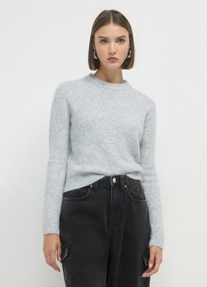 Pull en laine grise clair, texturé, avec un col rond et des manches longues, associé à un pantalon noir taille haute avec des poches latérales.