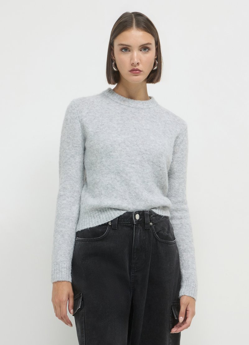 Helles graues, strukturiertes Sweatshirt mit rundem Halsausschnitt und langen Ärmeln, kombiniert mit hochgeschnittenen schwarzen Hosen mit seitlichen Taschen.