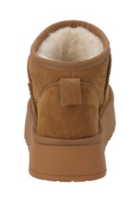 Bota de tobillo de ante marrón con un forro interior esponjoso, parte superior redonda y un tacón pequeño. Presenta una lengüeta trasera para facilitar el calzado.