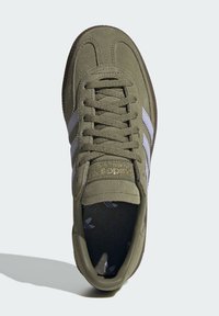 Sapatilhas de camurça verde-oliva com riscas cinzentas, bico arredondado e sola texturizada. Acento dourado na língua com marca. Design minimalista.